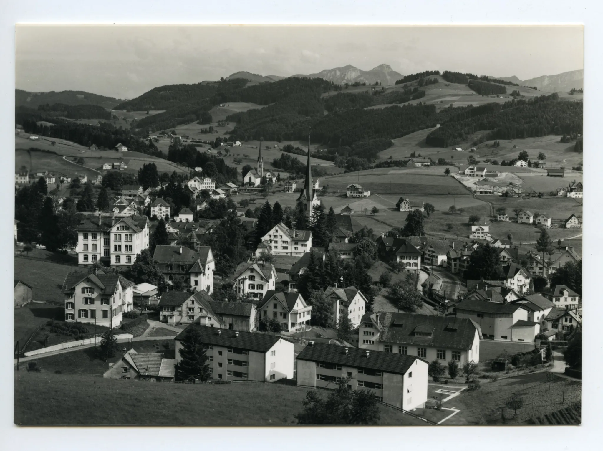 beide Dorfkirchen, SGA-Komposition zwischen Dorfplatz u. Drogerie Wetzel. Blick zum Steigbach, Kamor/Hohem Kasten. Vorne alte Turnhalle plus zwei neue MFH (zum Vergleich: Hc.17-26, Stempel 1954). Markante Baustelle/Neubau Schönenbüel (z.Vergleich ebenfalls Hc.17-26)