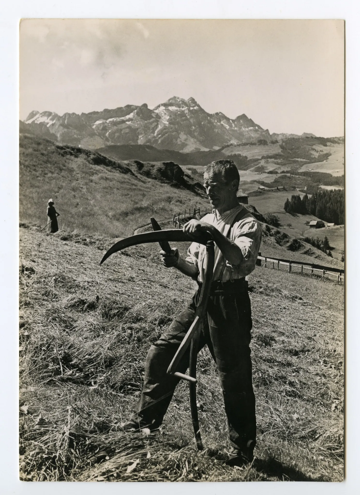 Ansicht von Bauer beim Schleifen der Sense auf dem Feld, mit Alpstein im Hintergrund