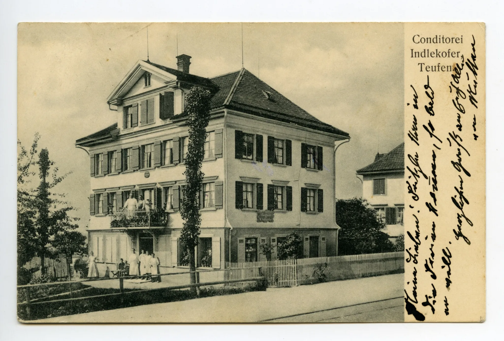 Ansicht mit Eigentümerehepaar? auf dem Balkon und Personal vor dem Haus, Bahnschienen sichtbar. (später Café Mettler, Hauptstrasse 21) (vgl. Hc.08-54, Karte identisch)