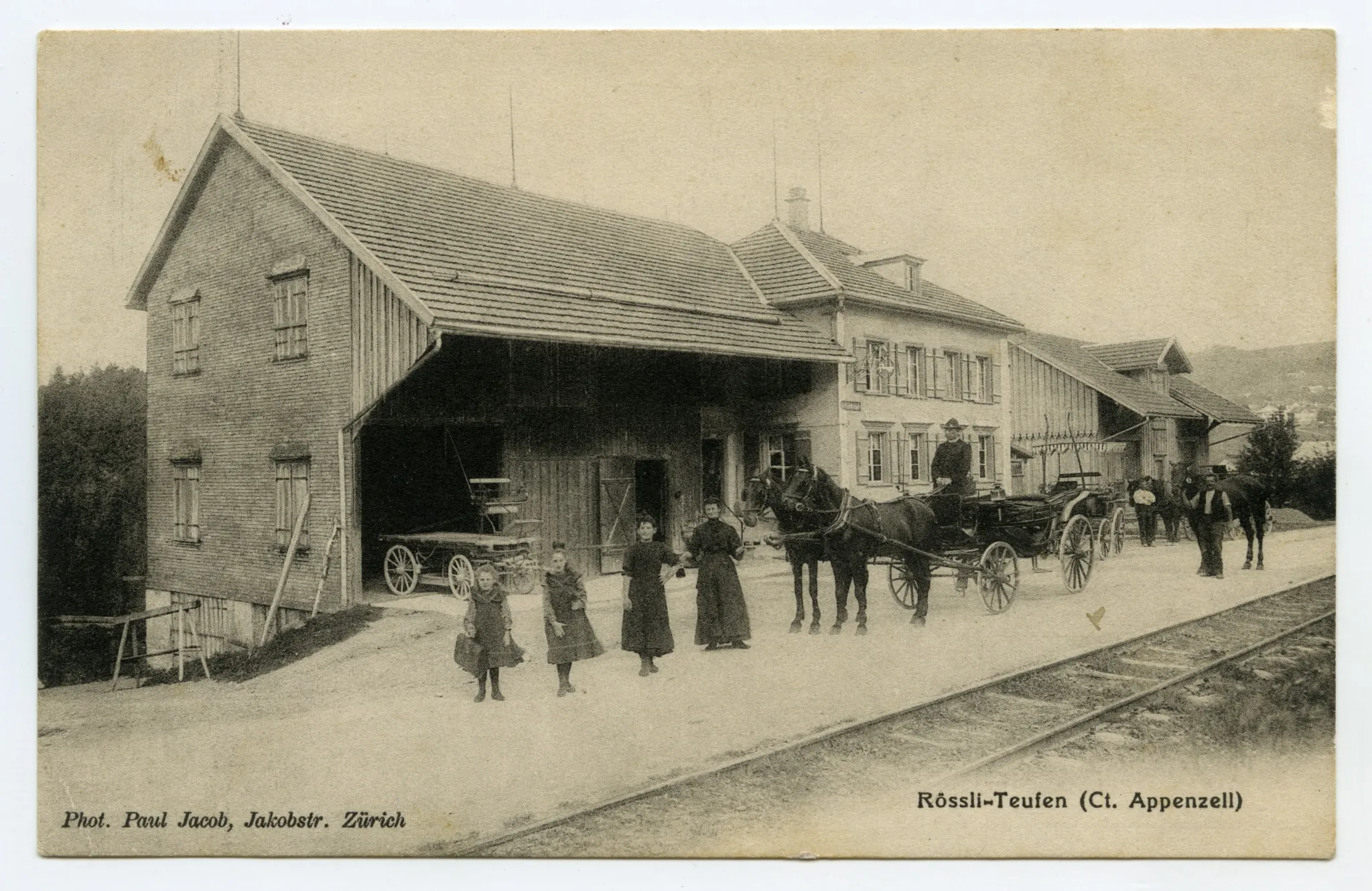 Ansicht aus Süden mit Bahngleis im Vordergrund, Personen und Pferdekutsche vor dem Haus
