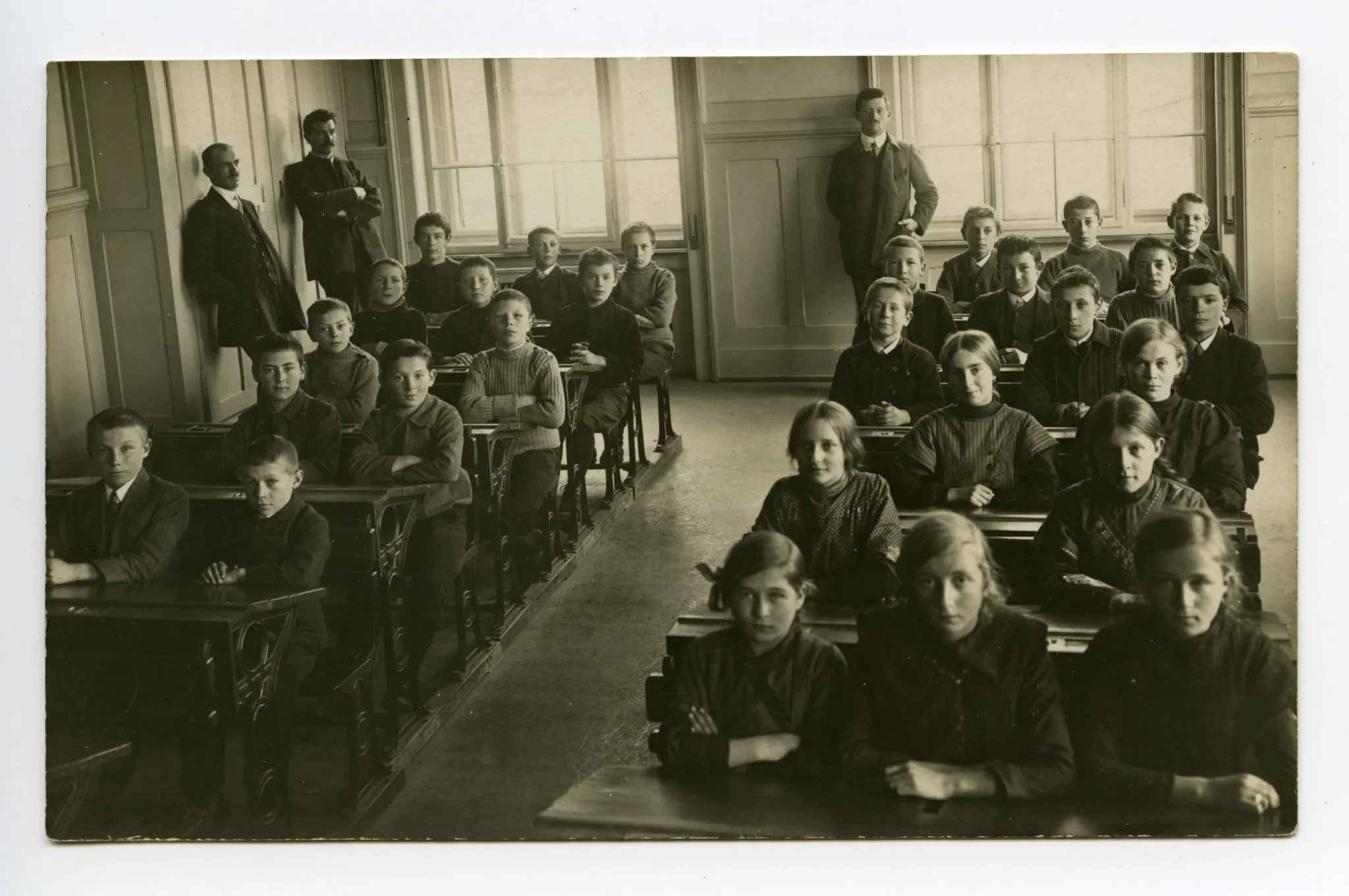 drei Lehrer mit Schülern und Schülerinnen sitzend in den Bänken (vgl. 01-04, gleiche Lehrer, aber andere Schulklasse, dat. 1913)