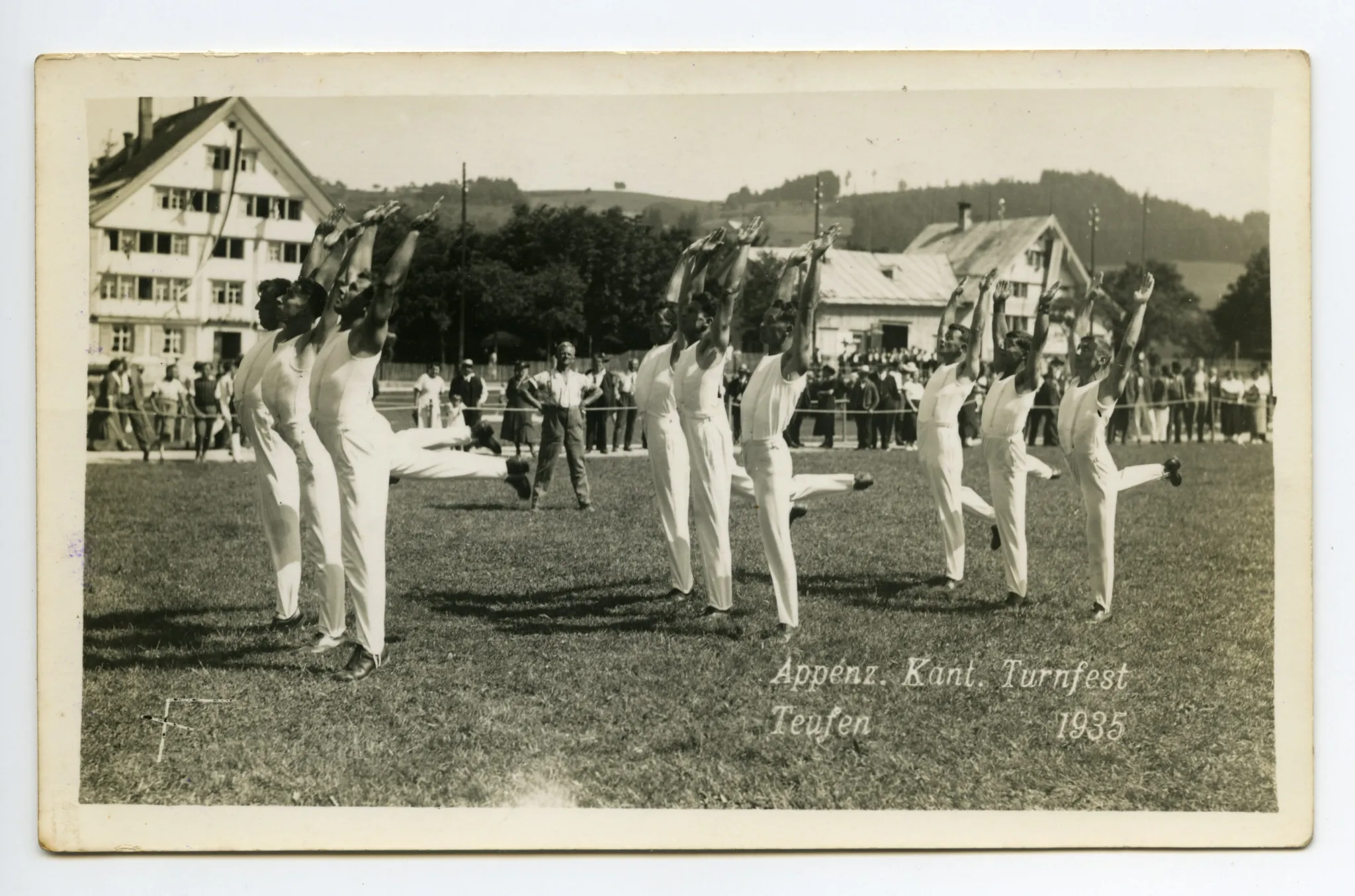 neun Turner synchron beim Turnen einer Übung auf dem Zeughausplatz, im Hintergrund Kinderkurhaus Sanitas