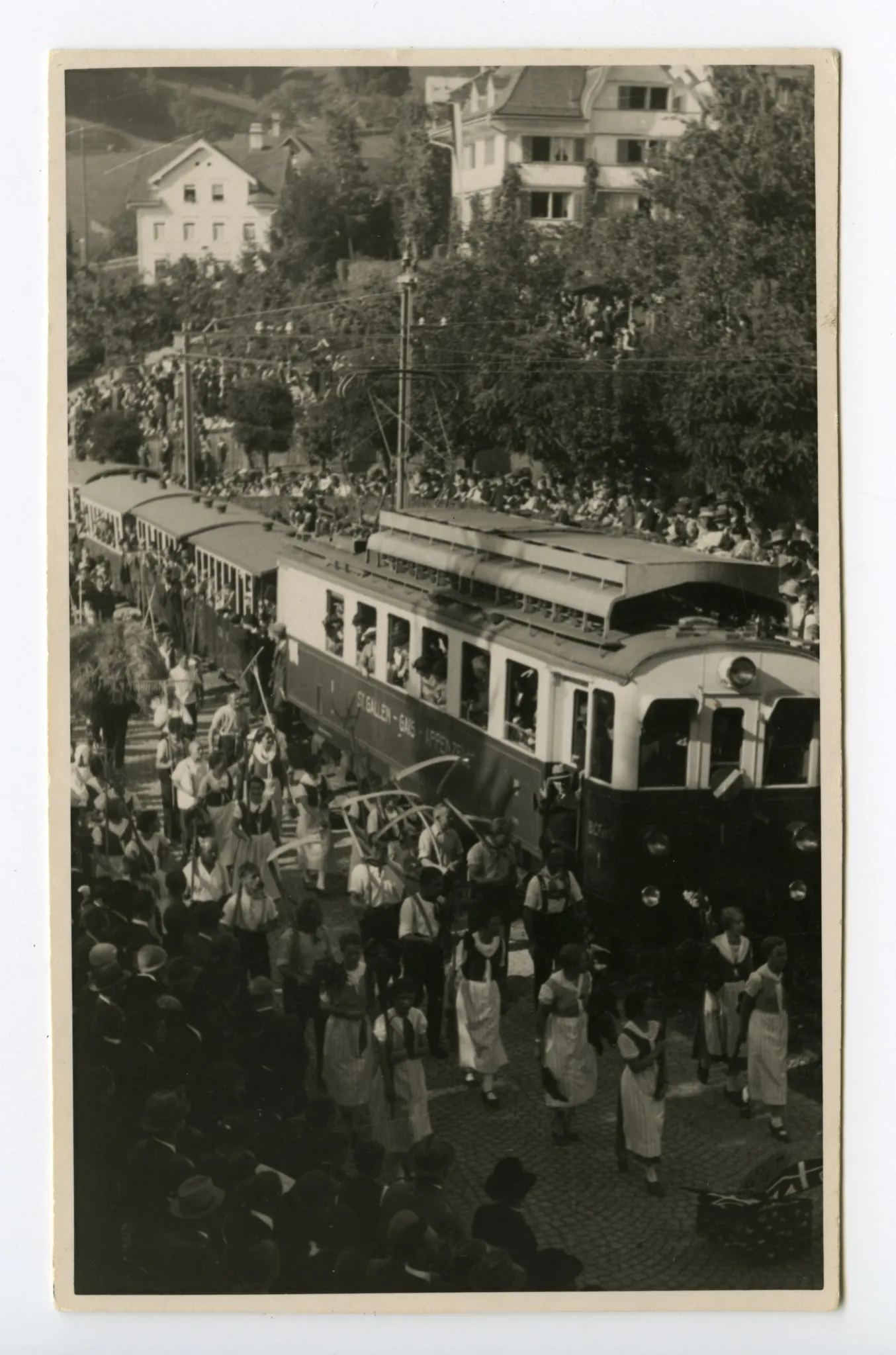 Gruppe der Bauern mit Sense und Bäuerinnen mit Rechen in der Kurve zum alten Bahnhof, fahrende Bahn (SGA)