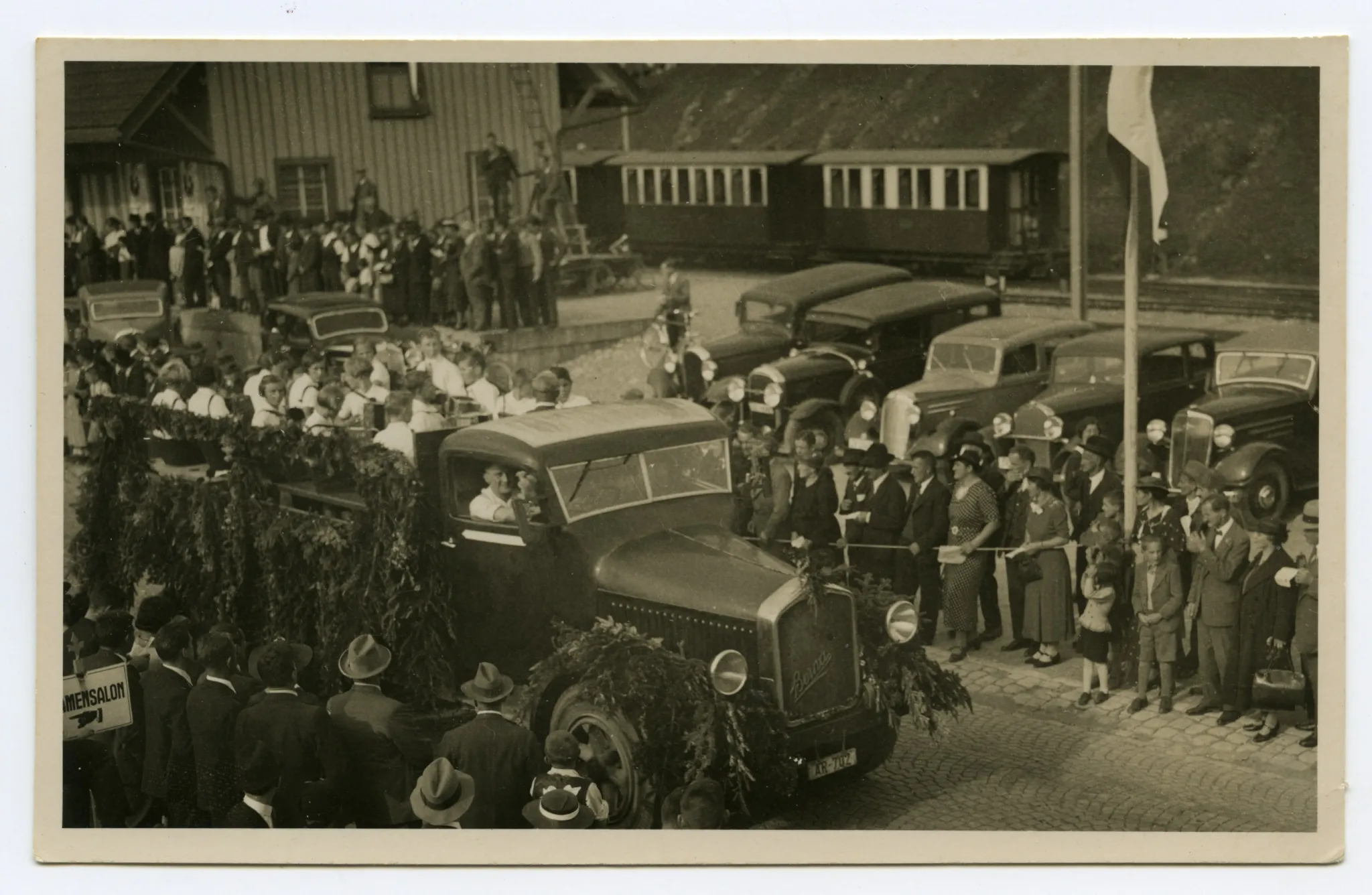 Lastwagen (Berna) mit Jugendharmonikerorchester, Sänger und Sängerinnen auf dem offenen Wagen, im Hintergrund Güterschuppen