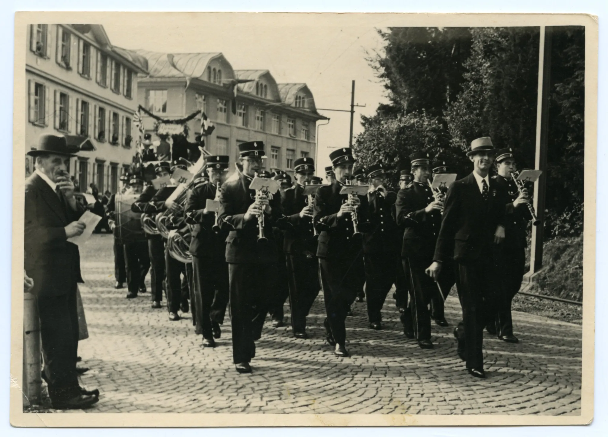 Gruppe einer Musikkapelle mit Musikanten und Dirigent, musizierend, im Hintergrund Kunz Druckerei