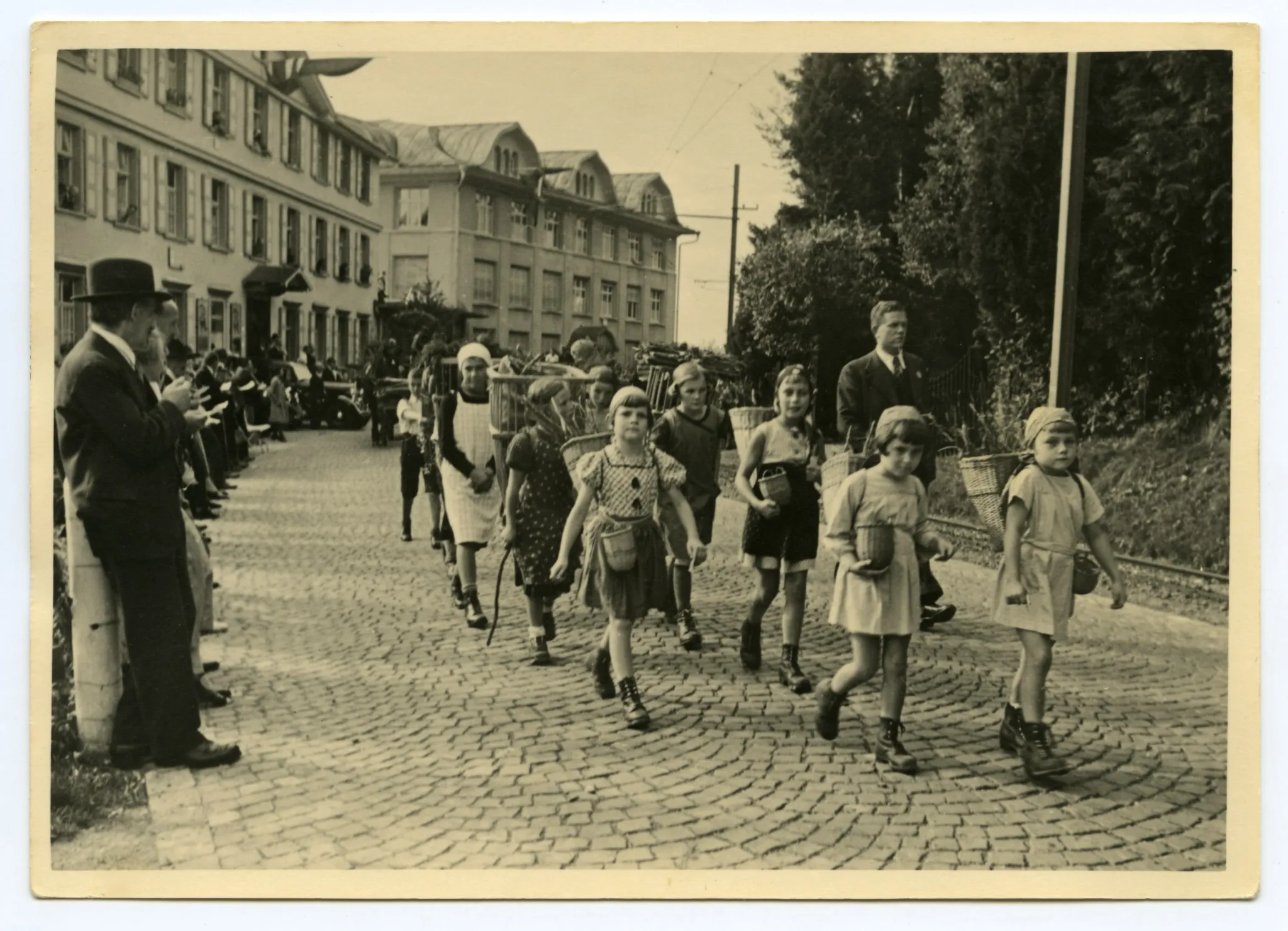 Gruppe von Kindern (Schüler)auf der Hauptstrasse gehend, Kinder mit Chränzen und Beerenkörgen, im Hintergrund Druckerei Kunz