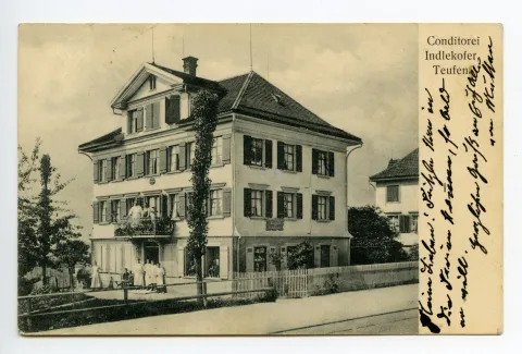 Ansicht mit Eigentümerehepaar? auf dem Balkon und Personal vor dem Haus, Bahnschienen sichtbar. (später Café Mettler, Hauptstrasse 21) (vgl. Hc.08-54, Karte identisch)