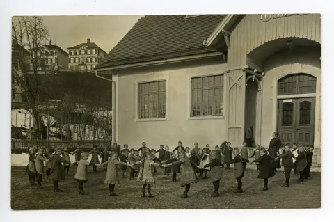 Kinder im Kinderreigen vor der Turnhalle mit Lehrperson