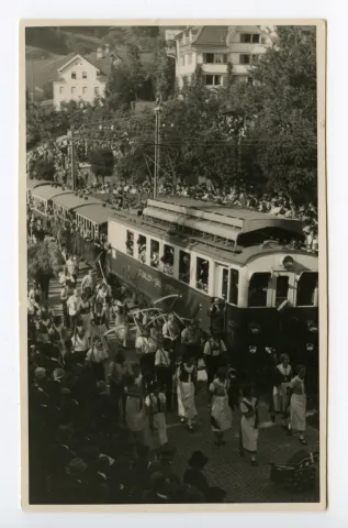 Gruppe der Bauern mit Sense und Bäuerinnen mit Rechen in der Kurve zum alten Bahnhof, fahrende Bahn (SGA)