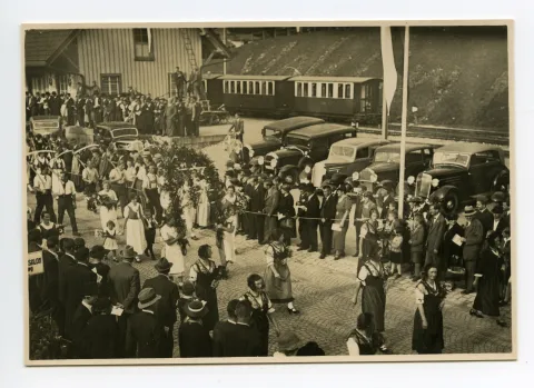 Gruppe der Bauern und Bäuerinnen vor dem Güterschuppen, vorauslaufend Trachtengruppe (vgl. Ho.30-038)
