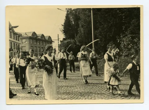 Gruppe der Bauern und Bäuerinnen laufend auf der Hauptstrasse, im Hintergrund: Gebäude Druckerei Kunz, Nahaufnahme