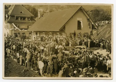 Fuhrwerk der Zimmerei mit arbeitenden Zimmerleuten auf dem Wagen, im Hintergrund Güterschuppen und Bahnhof