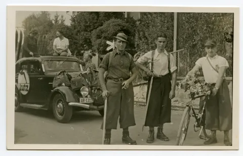 Gruppe des Sportgeschäfts „Lutz“, Nahaufnahme Gruppenbild mit zwei Wanderern und einem Velofahrer, im Hintergrund dekorierter Wagen